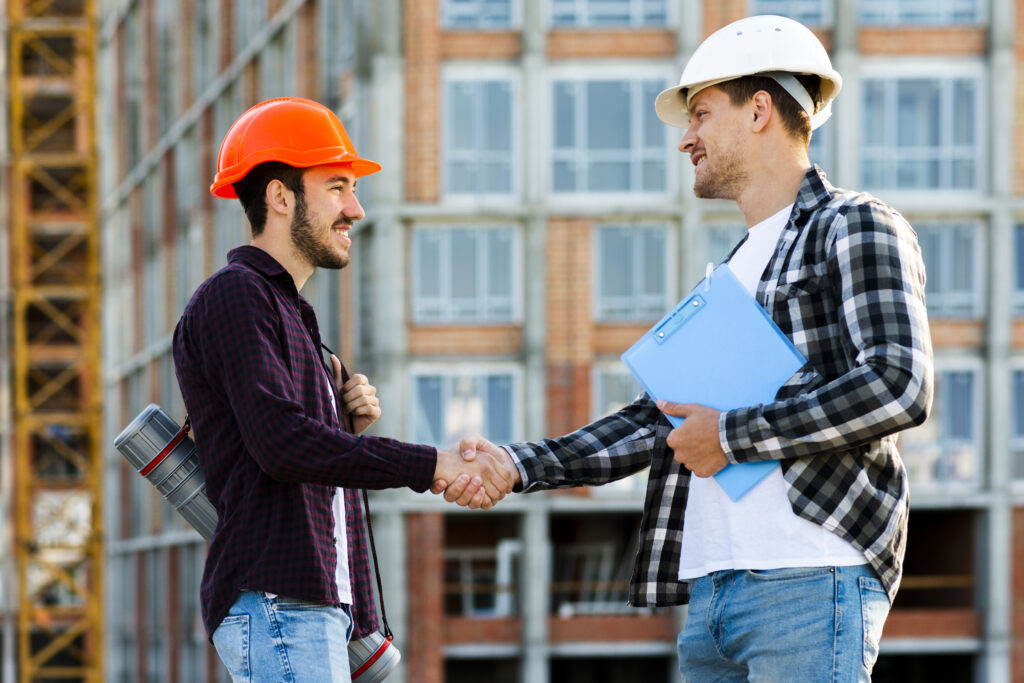 Construction engineer and skilled worker shaking hands at a job site symbolizing professional manpower services and workforce partnership.